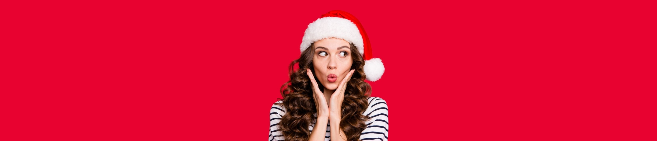 Girl in black and white striped long sleeved top, in front of a red background, wearing a christmas cap